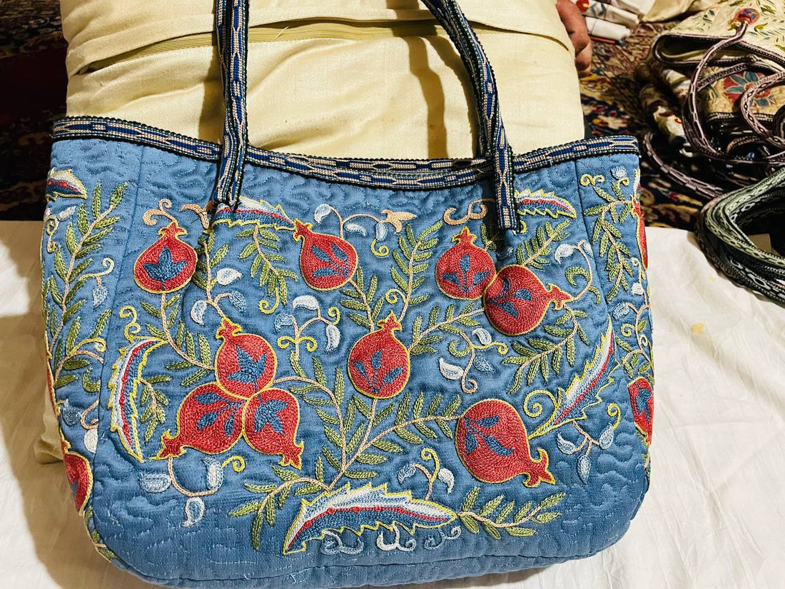 Blue embroidered handbag with red pomegranate and floral designs.